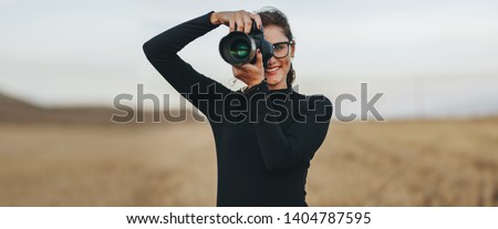 Professional female photographer with dslr camera photographing outdoors. Young woman with camera taking pictures.