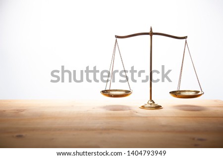 Gold brass balance scale on wooden desk and white backdrop, law and justice concept.