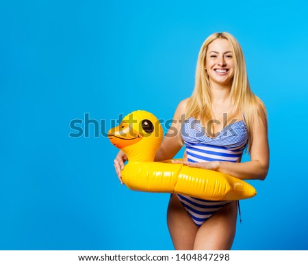 Picture of young blonde in striped swimsuit with life preserver at waist on empty blue background