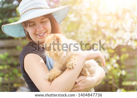 Photo of woman in hat with ginger cat in hands on blurred background