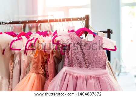 Rack with many beautiful holiday dresses for girls on hangers at children fashion showroom indoor. Kid girl dress hire studio for celebration birthday party or photography session event