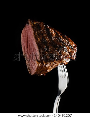grilled steak rib eye on a fork on black background Royalty-Free Stock Photo #140491207