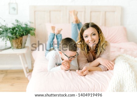 Young mother and son playing at home together. Home games on vacation. Happy sister and brother fooling on the bed. Scandinavian interior bedroom. Noisy photography concept. Soft focus photo