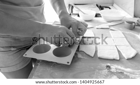 Black and white photo of young woman making cupcakes in silicone form on kitchen