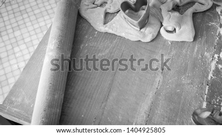 Closeup black and white photo of dough, flour and rolling pin lying on the wooden desk