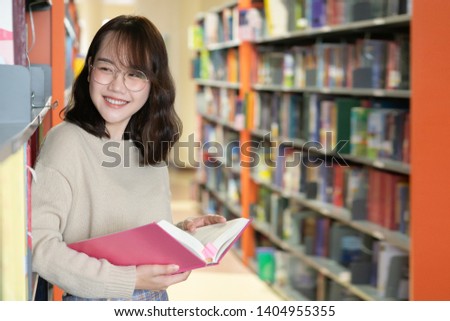 Happy Asian woman looking for a book in a library. Woman reading book in an university library. Library and Education concept.