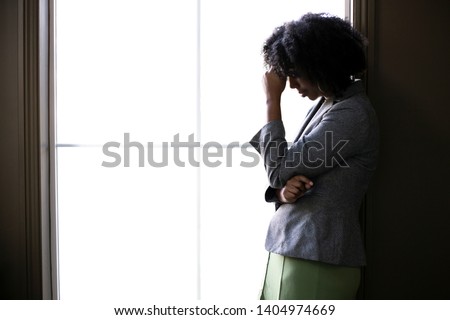Silhouette of a stressed out black African American businesswoman looking worried and thinking about problems and failure by the office window.  She looks depressed or upset about debt or bankruptcy. Royalty-Free Stock Photo #1404974669
