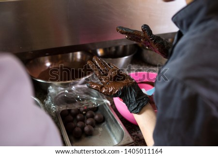 Theme cooking chocolates truffle. Close-up hand Young Caucasian woman and man cook with tattoo and in uniform prepares, makes round balltake the sweetness of cake. Confectioner covers raspberry puer.