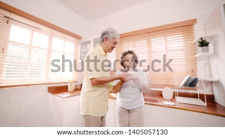 Asian elderly couple man holding cake celebrating wife's birthday in kitchen at home. Chinese couple enjoy love moment together at home. Lifestyle senior family at home concept.