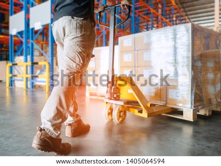 warehouse worker is working with hand pallet truck or pallet jack and cargo pallet. Royalty-Free Stock Photo #1405064594
