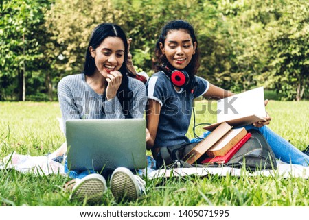 Group of smiling international students or teenagers sitting and using laptop computer doing their homework with book together in park at university.Education and friendship Concept