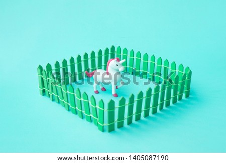 Cute unicorn horse toy model in fence on color background