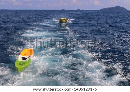 Kayak boat tied with rope and pulled by big boat in sea.