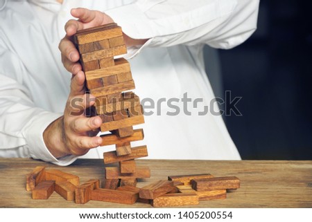 Businessman acting to stop destroy from wood block building,risk concept.