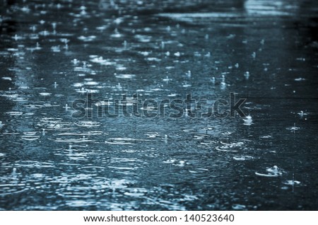 Rain drops rippling in a puddle with blue sky reflection Royalty-Free Stock Photo #140523640