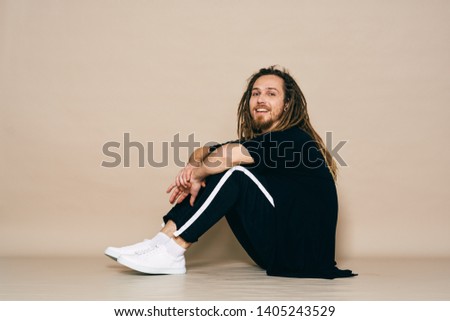 A handsome man sits on the floor in sneakers dark trousers and a T-shirt break dance dreadlocks                      