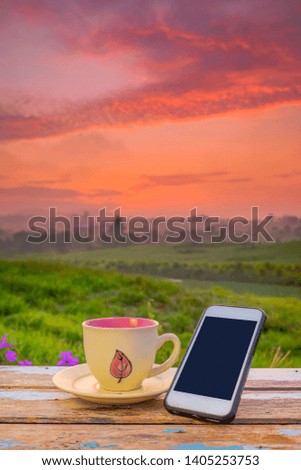 Black coffee cup and smartphone  on wooden table over blurred image of beautiful scenery