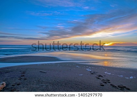 Background with sunset on the sea landscape: Sand beach with endless horizon and incredible foamy waves under the bright sundown with intense orange and red colors and clouds above the sea