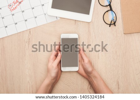 partial view of recruiter holding smartphone with blank screen at workplace