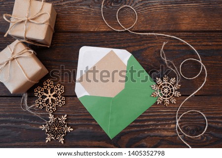 Christmas mockup holiday letter Blank paper in green envelope with wooden snowflakes and gift boxes on wood table, with space for your text, top view