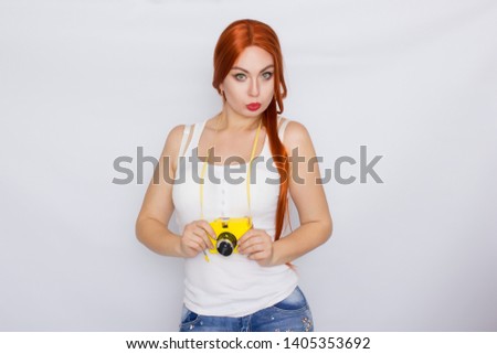 Happy pretty redhead woman wearing white tshirt making photo and looking at yellow camera over white background