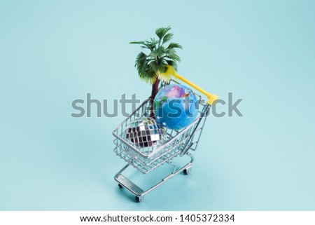 a disco ball, palm tree and a planet earth in a supermarket shopping cart turquoise on a turquoise background. Minimal still life color photography