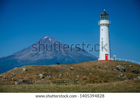 Cape Egmont Lighthouse with Mountain Taranaki in the background and blue sky above. Egmont National Park, New Zealand North Island