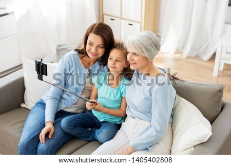 family, generation and technology concept - happy mother, daughter and grandmother taking picture by smartphone on selfie stick at home