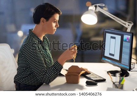 business, deadline and people concept - female graphic designer eating takeaway wok food by chopsticks and working on computer at night office