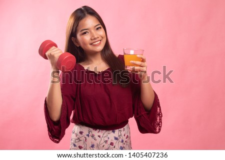 Young Asian woman with dumbbell drink orange juice on pink background
