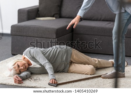 partial view of man near senior woman with walking stick lying on carpet