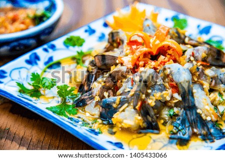 Raw Shrimps chilled in fish sauce on white dish with vegetable and red spicy sauce Viet food. They are decorated on wooden table background 
