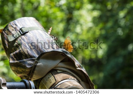 Butterfly flies and stands on Camouflage camera lens of photographer in forest