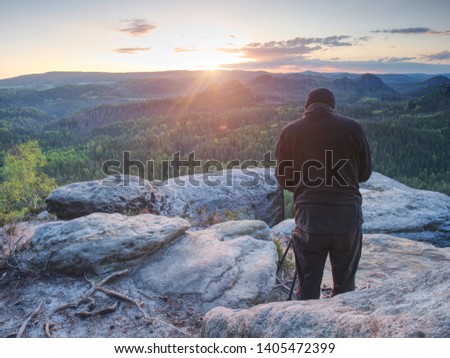 Tall adult photographer prepare camera for taking picture of fall mountains. Photograph at daybreak above colorful valley.