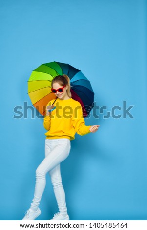  woman in glasses with an umbrella holds free hand on a blue background                             