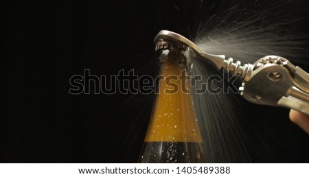 Opening cold bottle of beer with bottle opener. Cold beer on a black background. Craft light beer in bottle with condensate and water drops. Close-up shot