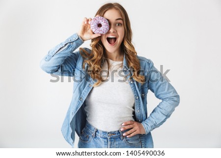 Attractive cheerful young girl standing isolated over white background, holding tasty donut