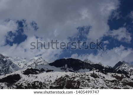 dark rocky mountains with snow over them in himachal pradesh india in winters with blue sky and clouds