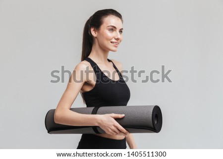 Image of a beautiful young sport fitness woman make exercises isolated over grey wall background holding fitness rug.