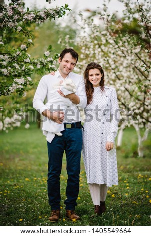 Mom and dad, daughter or son, young family outdoors in spring against the background of blooming apple and cherry trees. Happy parents in blossom garden.
