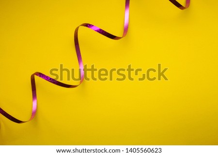 Close up of curved purple shiny ribbon on yellow backgound. Trendy minimalistic style, vibrant colors.