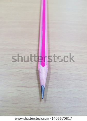 The pink pencil is on the table in the office.