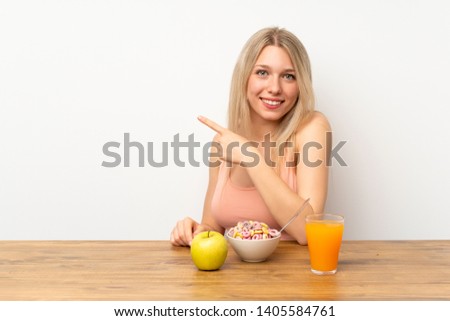 Young blonde woman having breakfast pointing finger to the side