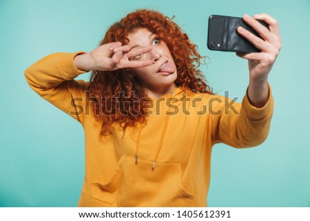 Portrait of an attractive redhead young woman standing isolated, taking a selfie, peace gesture