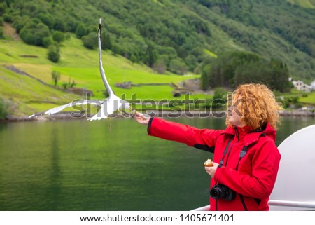 Woman in red jacket traveling on ferry boat and feeding seagull. Tourist feeds seagulls from the deck of the ship. Woman tourist on the deck of a ferry in Norway. Travel to Norway.