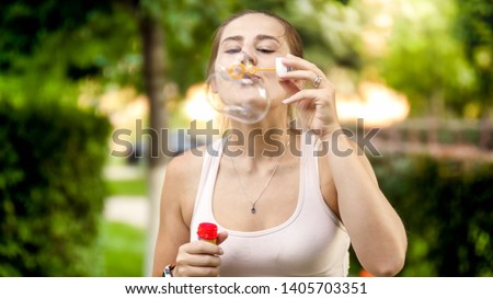 Portrait of happy smiling woman blowing colorful soap bubbles at summer park