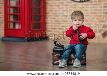 A little boy is talking on the phone near a red English phone booth. Language centre. Traveling around the world.