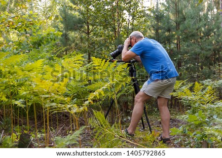 Male photographer with a camera engaged in shooting in the forest.