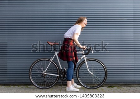 beautiful young girl standing with a white bicycle on a background of gray striped wall, the woman is happy and cheerful