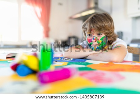 Cheerful child painting with colorful paint in the kitchen of his house